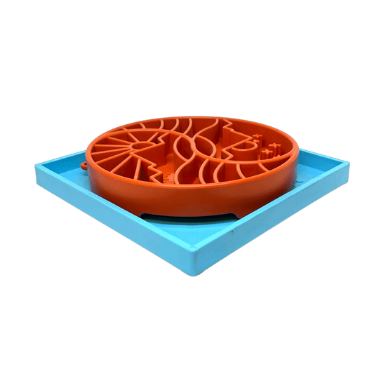 Orange circular slow feeder maze bowl on light blue rectangular suction cup base white background