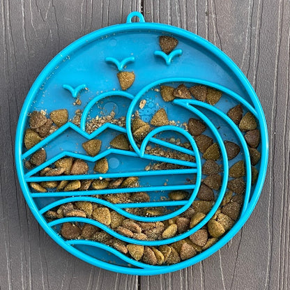 Blue slow feeder bowl filled with kibble on wood surface