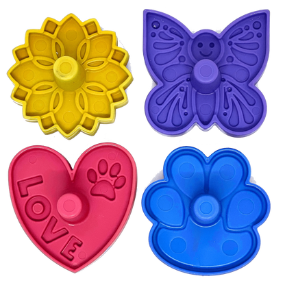 Four colorful plastic treat dispenser accessories featuring smiley butterfly, sunflower, heart with LOVE text, and paw shapes for upright freezing
