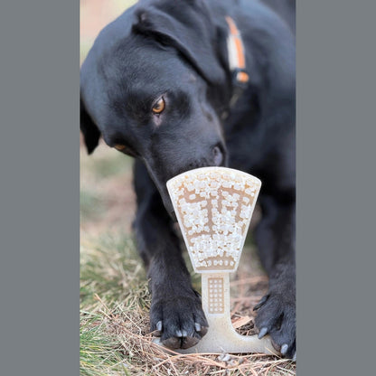 Black dog eating from textured waffle tower puzzle feeder on grass outdoors